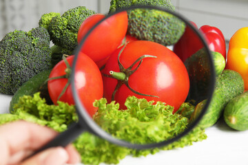 Wall Mural - woman with magnifying glass exploring vegetables, closeup. poison detection
