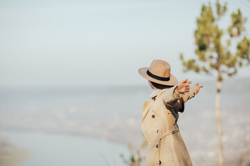 Wall Mural - Young woman standing with hands up on the top of the mountain and looking at the city from above.