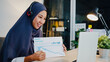 © tirachard - Asia muslim lady wear headphone using laptop talk to colleagues about sale report in conference video call while working from home office at night. Social distancing, quarantine for corona virus.