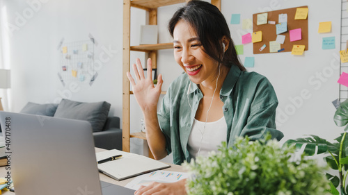 Asia businesswoman using laptop talk to colleagues about plan in video call while smart working from home at living room. Self-isolation, social distancing, quarantine for corona virus prevention.