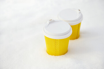 Two yellow takeaway paper cups with hot drink on a white fluffy snow in the winter park