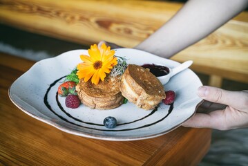 Fried Shepherd cheese with cranberry on a plante in hand. Dinner appetizer on a wooden table. Traditional polish cuisine