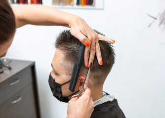 Male client getting a haircut wearing mask during coronavirus pandemic