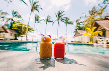 Fruit Cocktails In Glasses Decorated With Orchids By The Pool Overlooking The Tropical Sea And Palm Trees
