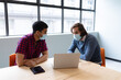 © WavebreakMediaMicro - Two diverse businessmen wearing face masks using laptop and discussing in creative office