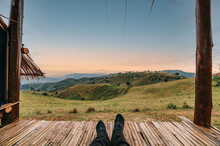 Legs Of Traveler Relaxing In Hut On Green Hill At Sunrise