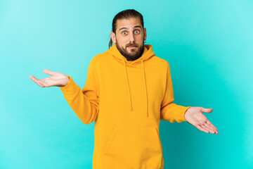 Young man with long hair look confused and doubtful shrugging shoulders to hold a copy space.