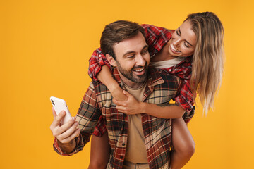 Wall Mural - Happy man using cellphone while piggyback riding his smiling girlfriend