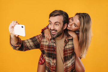 Wall Mural - Excited man taking selfie on cellphone while piggyback riding his girlfriend