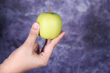 hand holding green apple on black background 