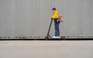 Wall Mural - Modern teenager with backpack rides on electric scooter. Boy comes back from school