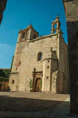 Wall Mural - Gothic church facade with decorated wooden door in front of small square on a sunny day at Cáceres. A fully preserved medieval town in Spain.