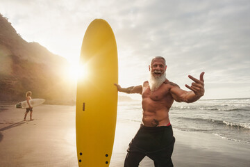 happy fit senior having fun surfing at sunset time - sporty bearded man training with surfboard on t