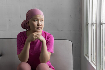 Young adult female cancer patient wearing headscarf sitting looking out window.