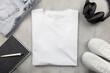 White womens cotton Tshirt mockup with jeans and sneakers, notebook and black headphones. Design t shirt template, print presentation mock up. Top view flat lay. Concrete stone background.