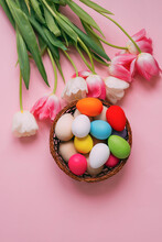 Happy Easter. Pink, White Tulips, A Basket With Colored Easter Eggs On A Rose Background. Vertical Photo.