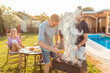 © Impact Photography - Men grilling meat while women are  sitting and relaxing by the pool at backyard barbecue party