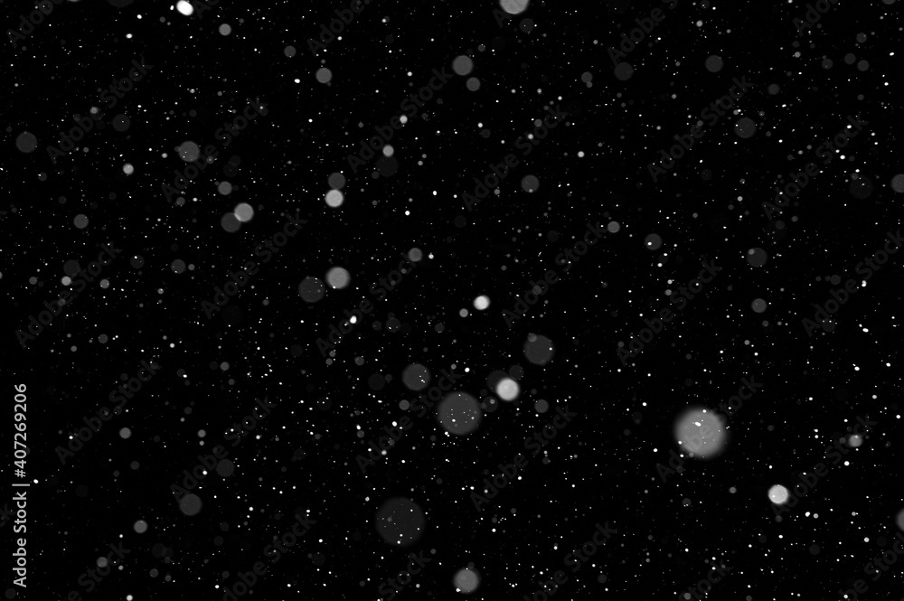 Bokeh of white snow on a black background. Falling snowflakes on night ...