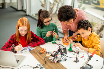 Wall Mural - Happy kids with their African American female science teacher with laptop programming electric toys and robots at robotics classroom