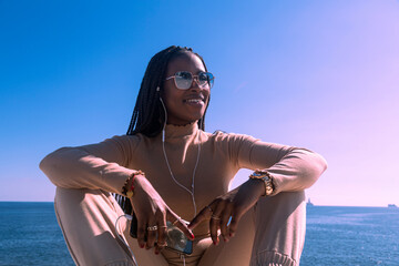 Closeup portrait of young black afro girl smiling with headphones and blue sky background, pretty afro girl transmitting positivity and peace.