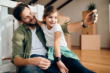 Wall Mural - Happy single father and his daughter taking selfie after moving into new home.