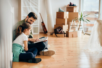 Wall Mural - Happy father and daughter looking at photo album while relocating in new home.