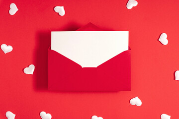 Creative minimal Valentine's Day concept. Red envelope with blank paper, valentines, white  hearts confetti on red background. Flat lay, top view, copy space