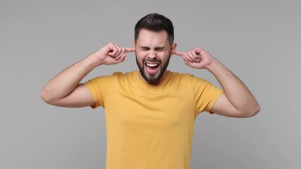 Canvas Print - Concerned frustrated bearded young man 20s in yellow casual basic t-shirt isolated on grey color background studio. People lifestyle concept. Covering ears with fingers keeping eyes closed screaming