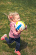 Happy running beautiful child girl with ball having fun outdoors symbolizing happy carefree childhood lifestyle