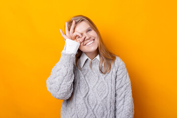 Photo of cheerful young woman in sweater making OK GESTURE over yellow background.