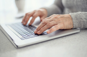 Hands of a woman senior work at a laptop close-up using modern technology in everyday life.