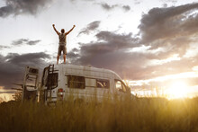 Man With Raised Arms On The Roof Of His Camper Van