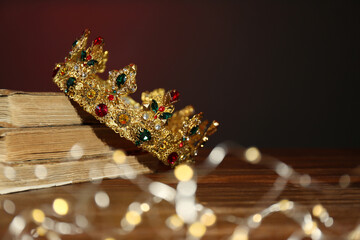 Wall Mural - Beautiful golden crown, old books and fairy lights on brown background. Fantasy item