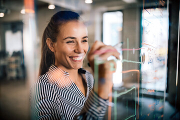 Woman working and writing on the glass board in office. Business, technology, research concept