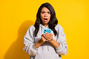 Poster - Photo of sad impressed dark skin woman wear grey hoodie chatting modern device isolated yellow color background