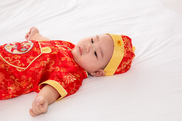 Wall Mural - Adorable Asian Chinese healthy baby lie down on bed looking for mom feeding, happy cute boy infant playing alone feeling happy, Chinese New Year wealthy prosperous Traditional Festival concept