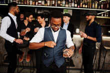Stylish African American Man Against Group Of Handsome Retro Well-dressed Guys Gangsters Spend Time At Club, Drinking On Bar Counter. Multiethnic Male Bachelor Mafia Party In Restaurant.