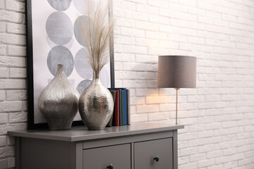 Sticker - Grey chest of drawers with decor and books near white brick wall. Interior design