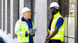 © NVB Stocker - Two engineers African american engineer and caucasian electrician wearing white hard hat walk in new building holding solar panel on hand and Discuss Work
