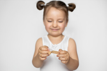 Happy little satisfied kid girl, wearing white tank top, with two ponytails, opening medical adhesive plaster bandage, smiling and looking at her hands. Close up shot. Focus on hands