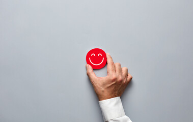 Businessman hand holding a red badge with a smiling face icon. Customer satisfaction or positive feedback