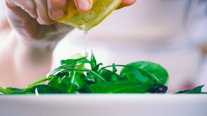 Wall Mural - Squeezing lemon on fresh salad. Chef preparing a dish full of green leaves of salad. Organic vegetable, natural ingredients for healthy nutrition.