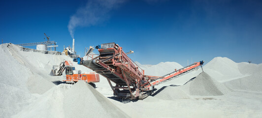 Wall Mural - Mobile crusher machine and excavator on the background of crushed stone hills and blue sky, panorama.