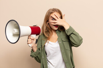 Wall Mural - blonde woman looking shocked, scared or terrified, covering face with hand and peeking between fingers