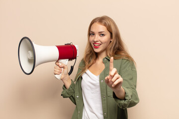 blonde woman smiling proudly and confidently making number one pose triumphantly, feeling like a leader