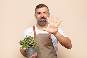 adult man smiling and looking friendly, showing number five or fifth with hand forward, counting down