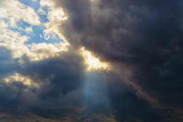 Wall Mural - san ray breaks through the gap in a large dark cloud covering the blue sky. changing weather from cl