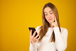 © Danko - Smiling business woman thinking with a smartphone over yellow background