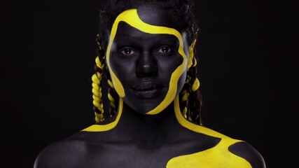 Wall Mural - Face art. Woman with black and yellow body paint. Young african girl with colorful bodypaint. An amazing afro american model with yellow makeup. Closeup face.