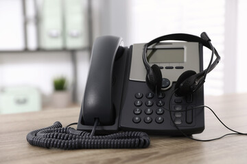 Desktop telephone and headset on wooden table in office. Hotline service